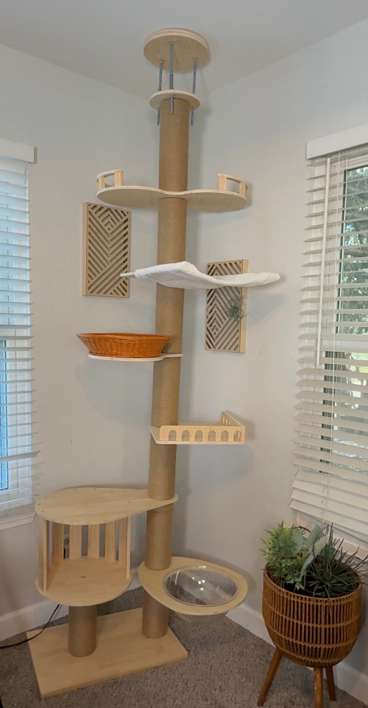 Cat tree with multiple levels, shelves, and a bowl in a room with windows and a plant.